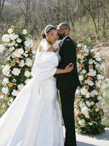A bride and groom standing in front of a floral arch