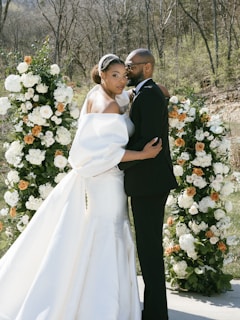 A bride and groom standing in front of a floral arch
