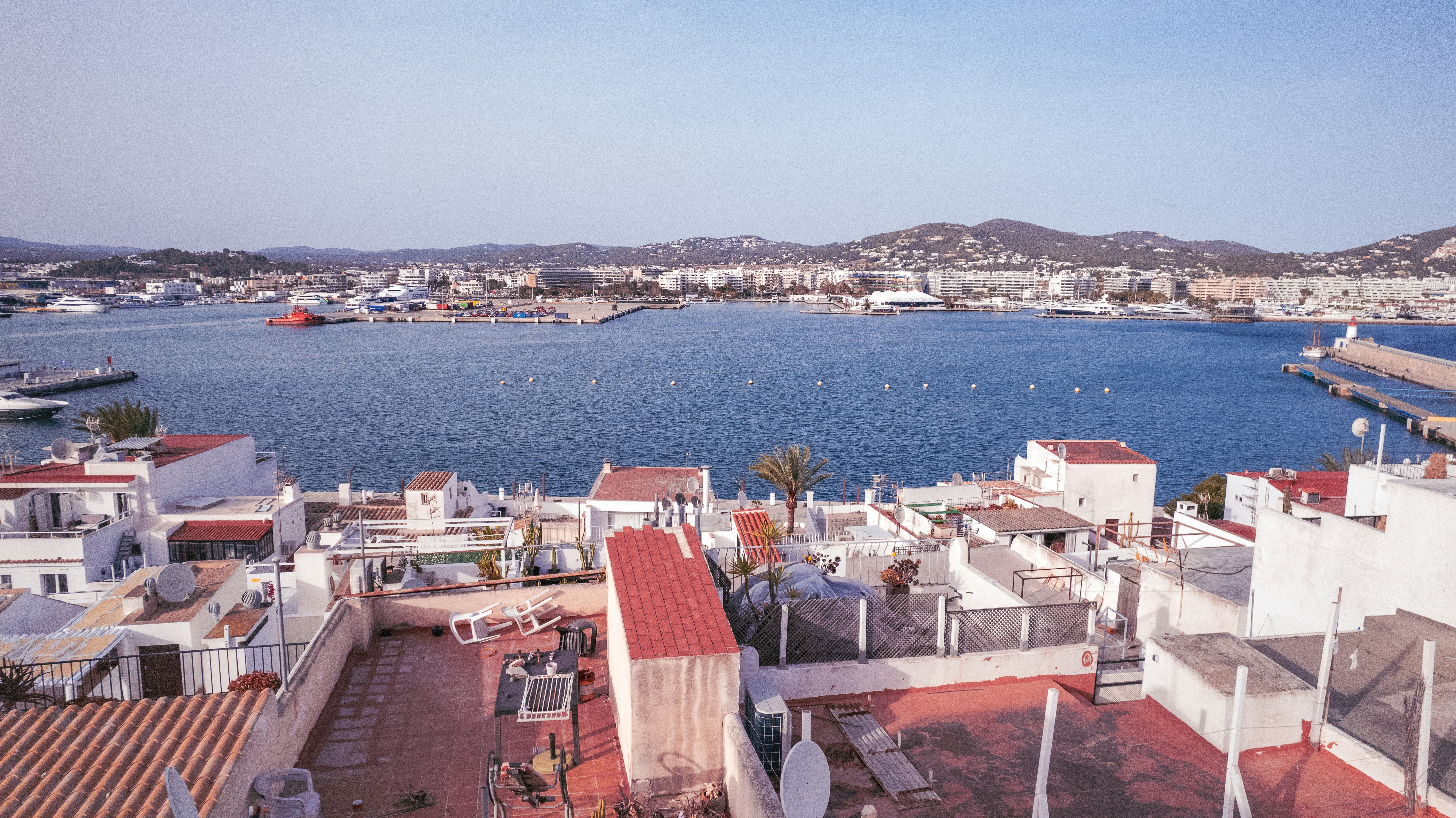 A view of a harbor from a rooftop of a building, Sa Penya Sa Penya is a district of Ibiza, situated at the far east of the original city. It extends between the bastion of Santa Lucia and the old harbour, bordering the quarters of La Marina and Dalt Vila. Between carrer Alt and Vista Alegre the topography drops 30 m above sea level until the corner with the “Baluard” of Santa Lucia.