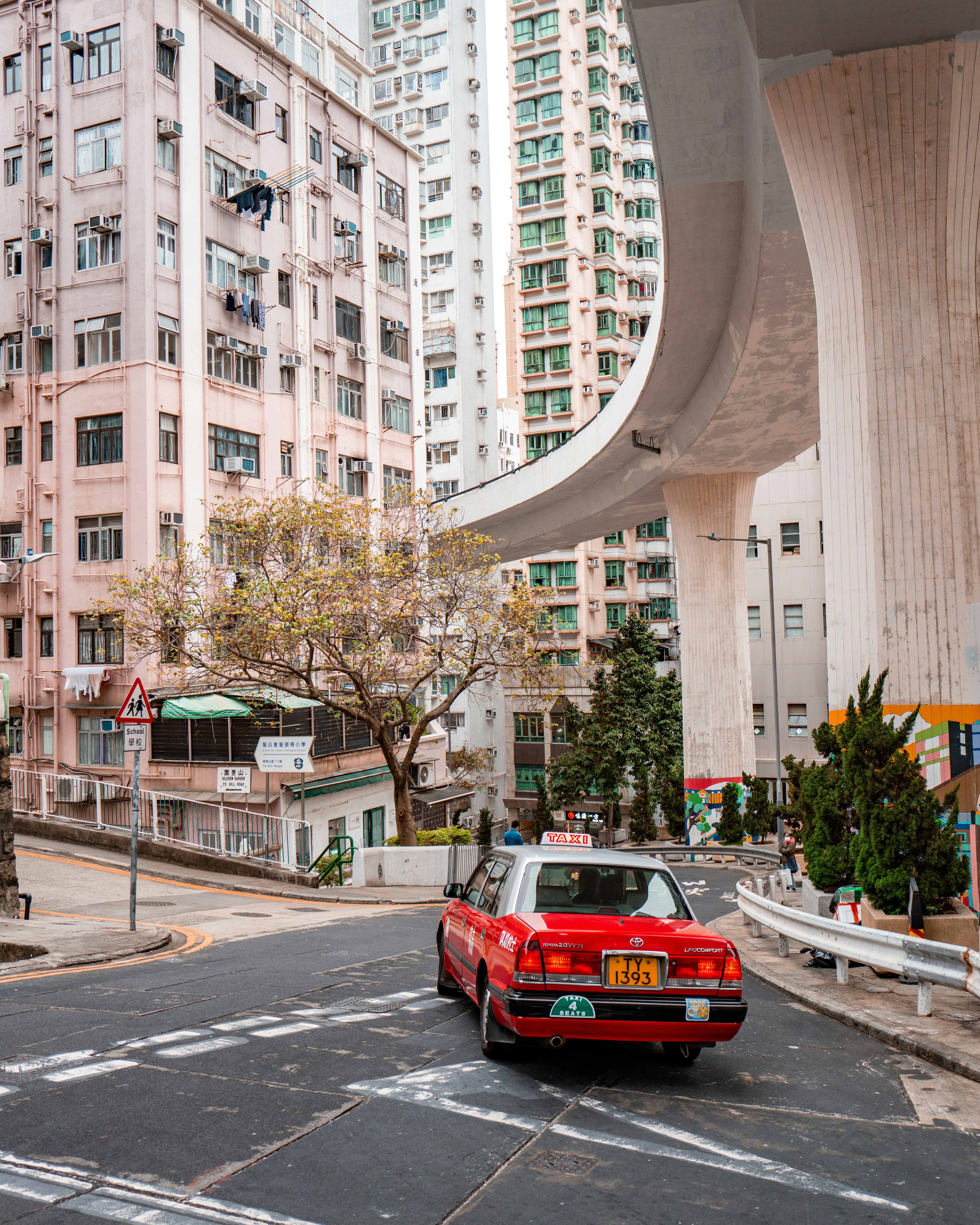 A red car driving down a street next to tall buildings