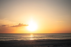 The sun is setting over the ocean on the beach