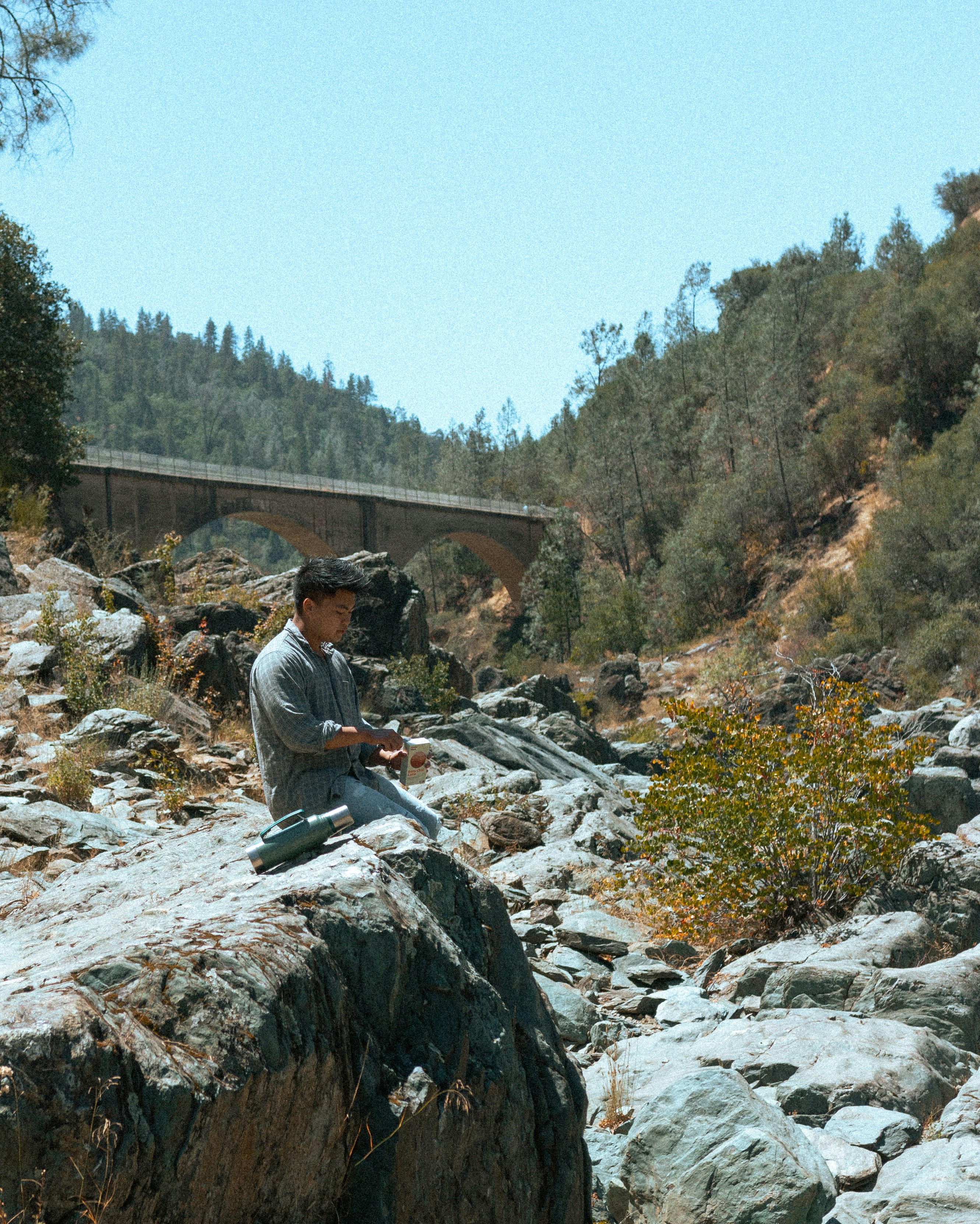 A man sitting on top of a rock next to a river