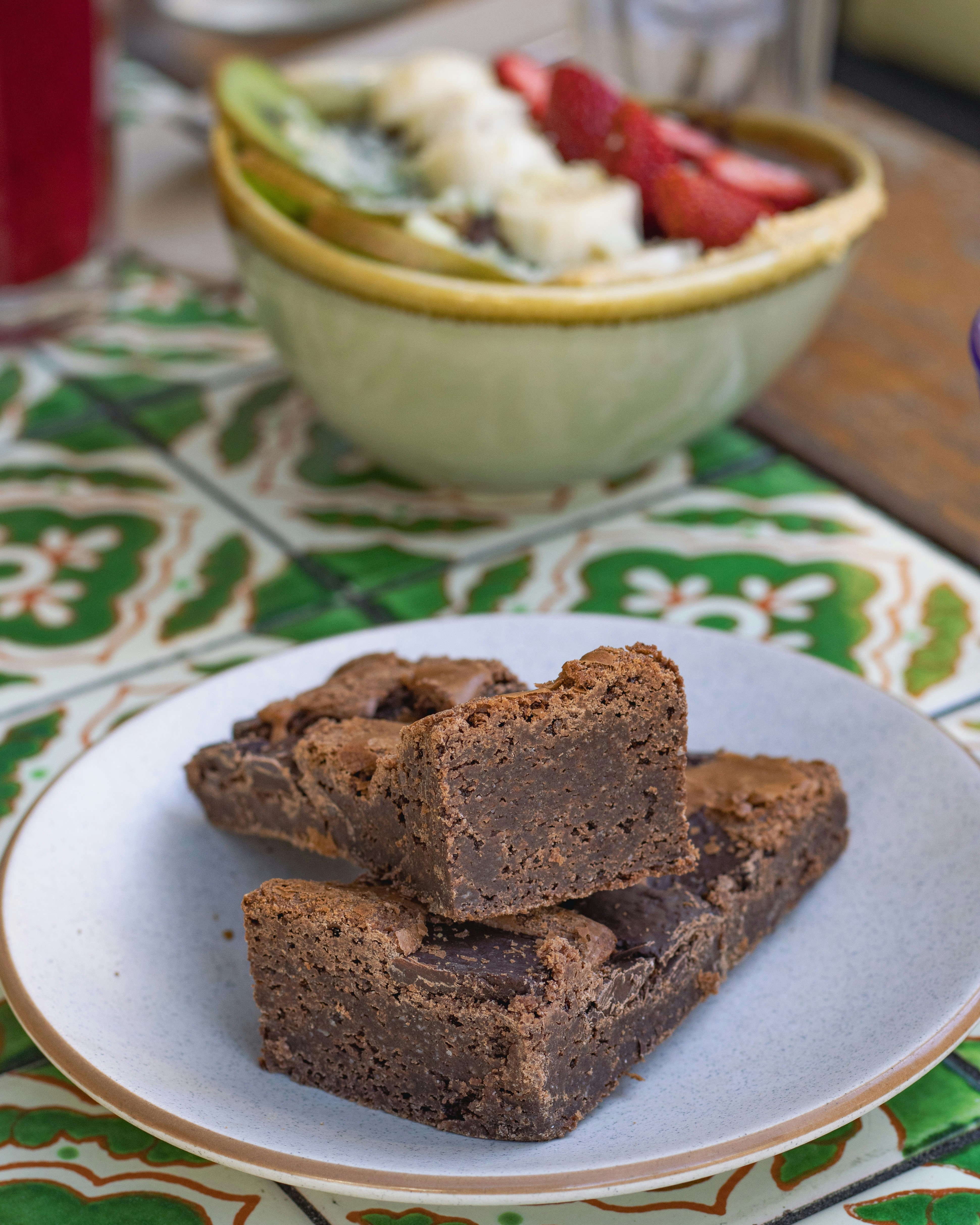A white plate topped with brownies next to a bowl of fruit