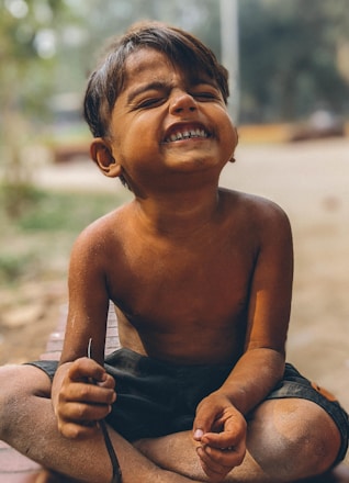 A young boy sitting on the ground with a toothbrush in his mouth