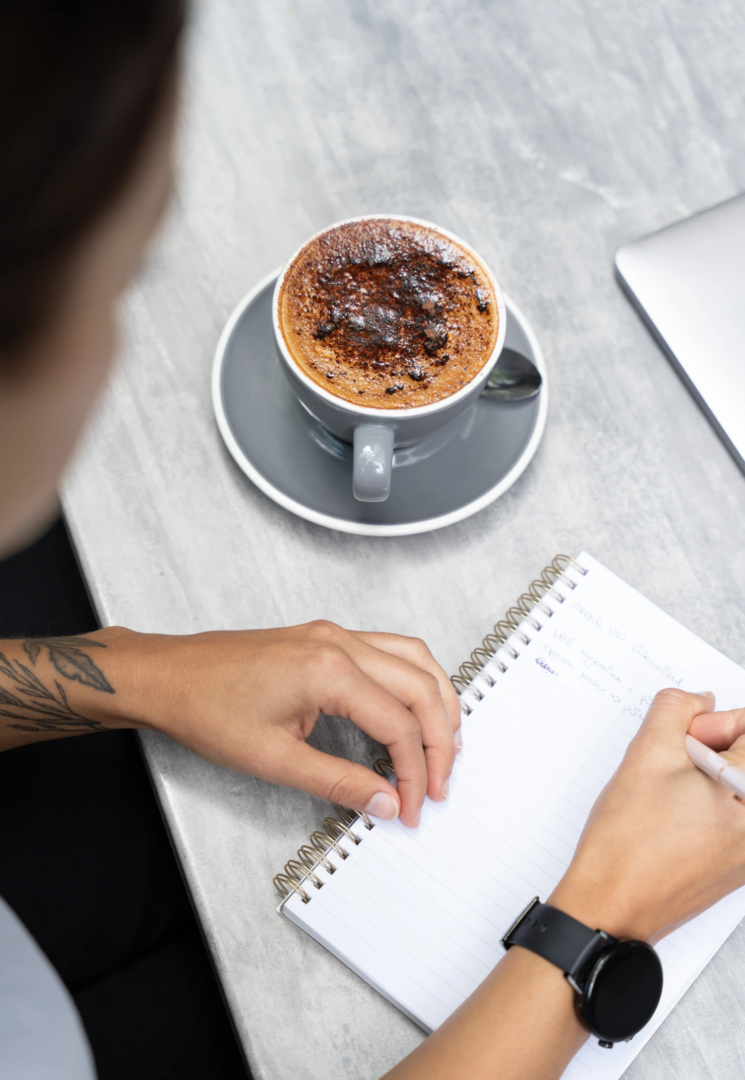 Person schreibt neben einer Tasse Kaffee in ein Notizbuch als Symbol für persönliche Ziele