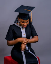 A woman sitting on a stool wearing a graduation cap and gown