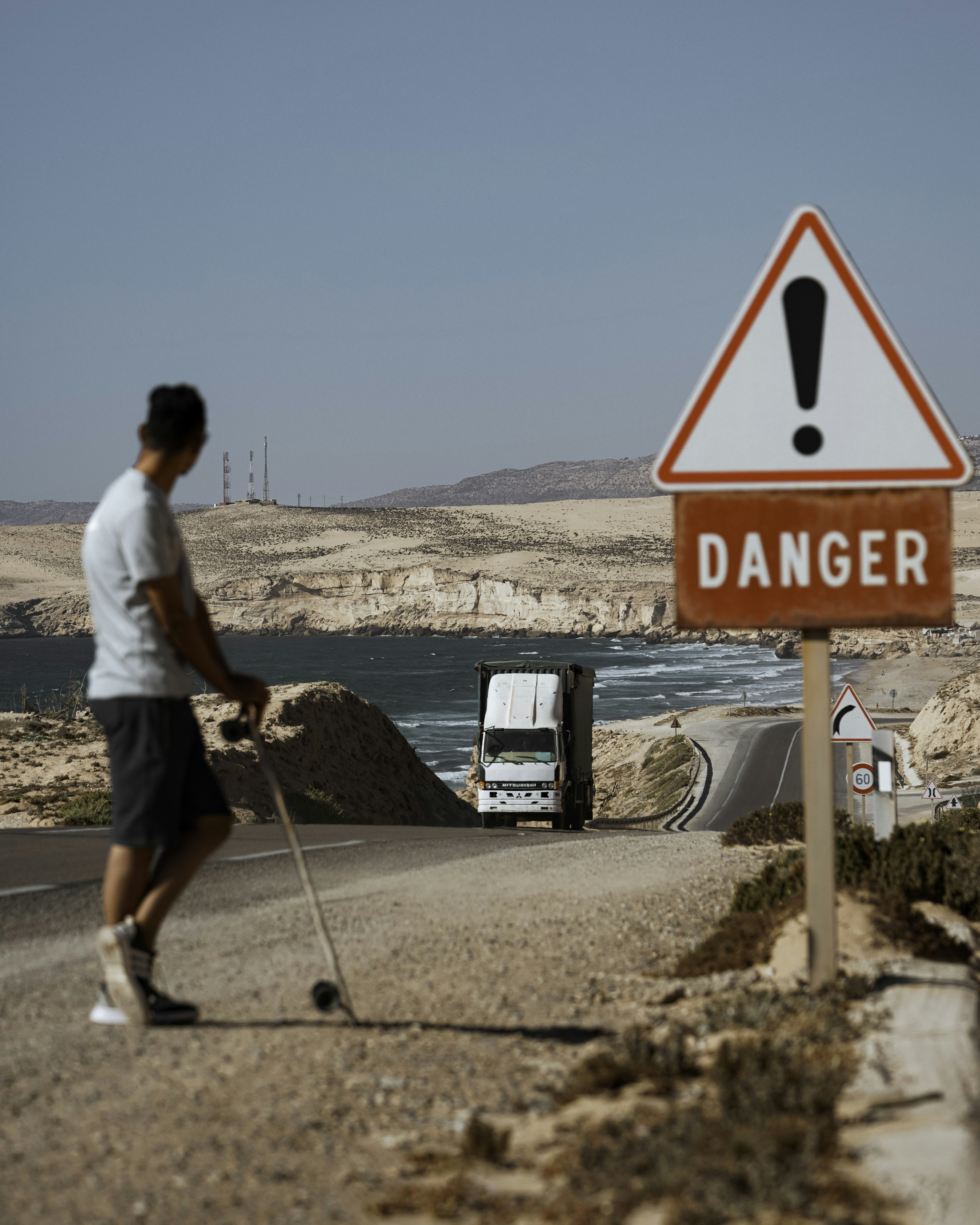 A man with a cane walks down a road next to a danger sign