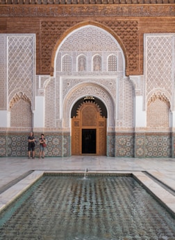 Two people standing in front of a building with a fountain