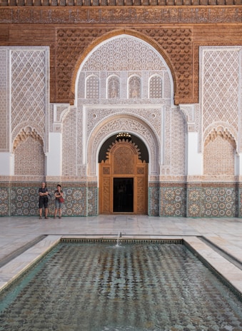 Two people standing in front of a building with a fountain