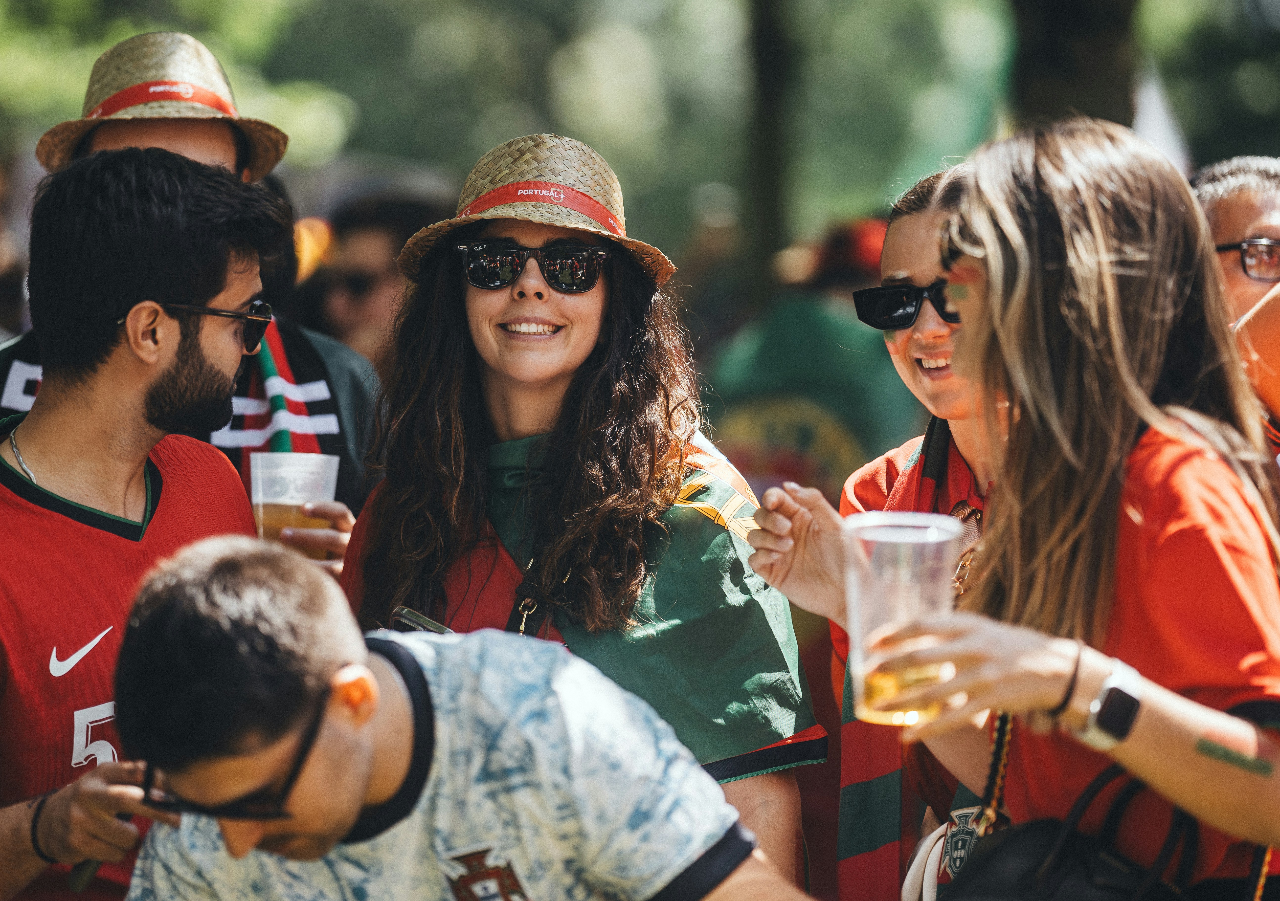Friends wearing Portugal hats and red clothing socialize outdoors while holding drinks.