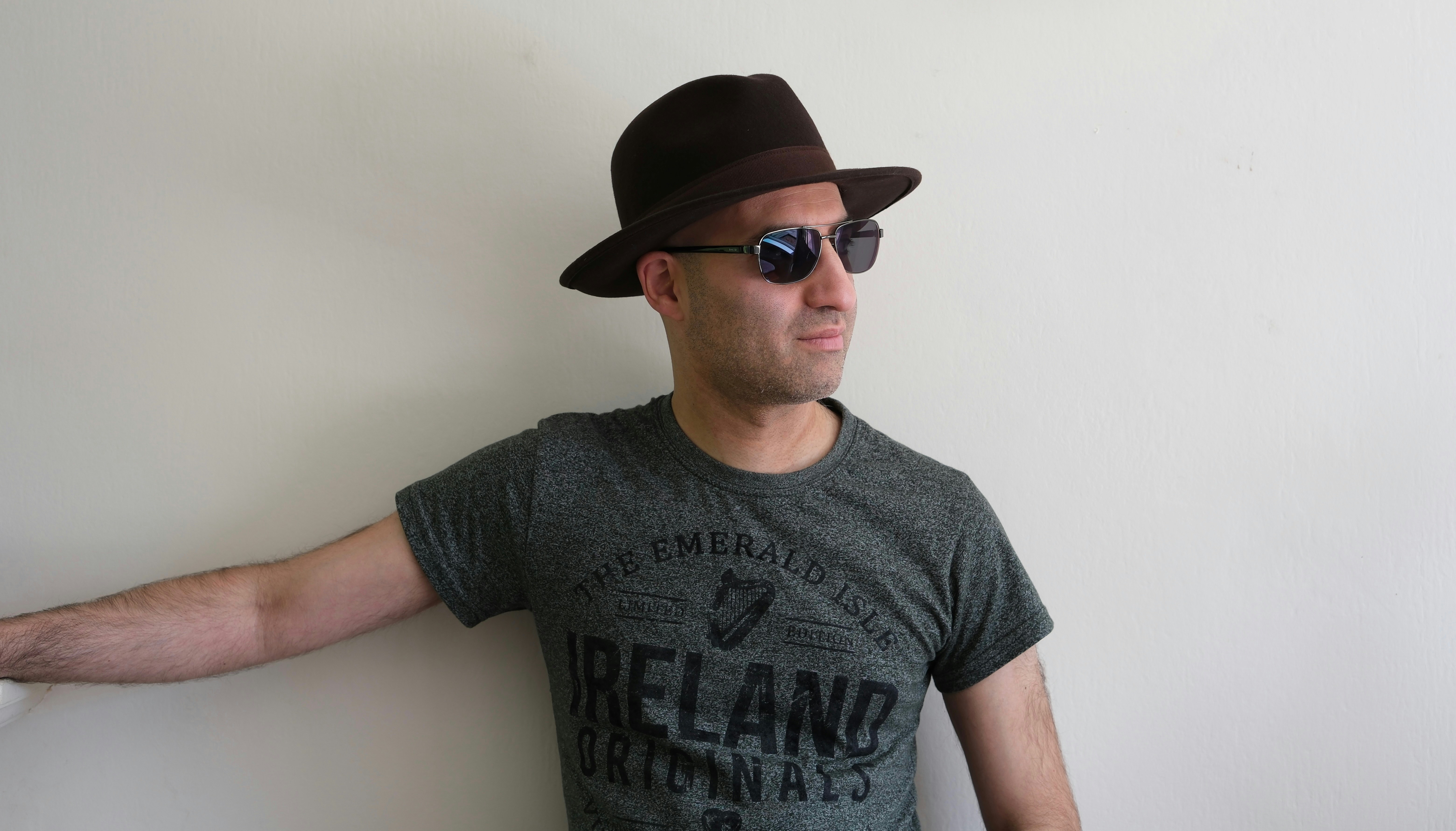 A man wearing a hat and sunglasses leaning against a wall photo – Free ...