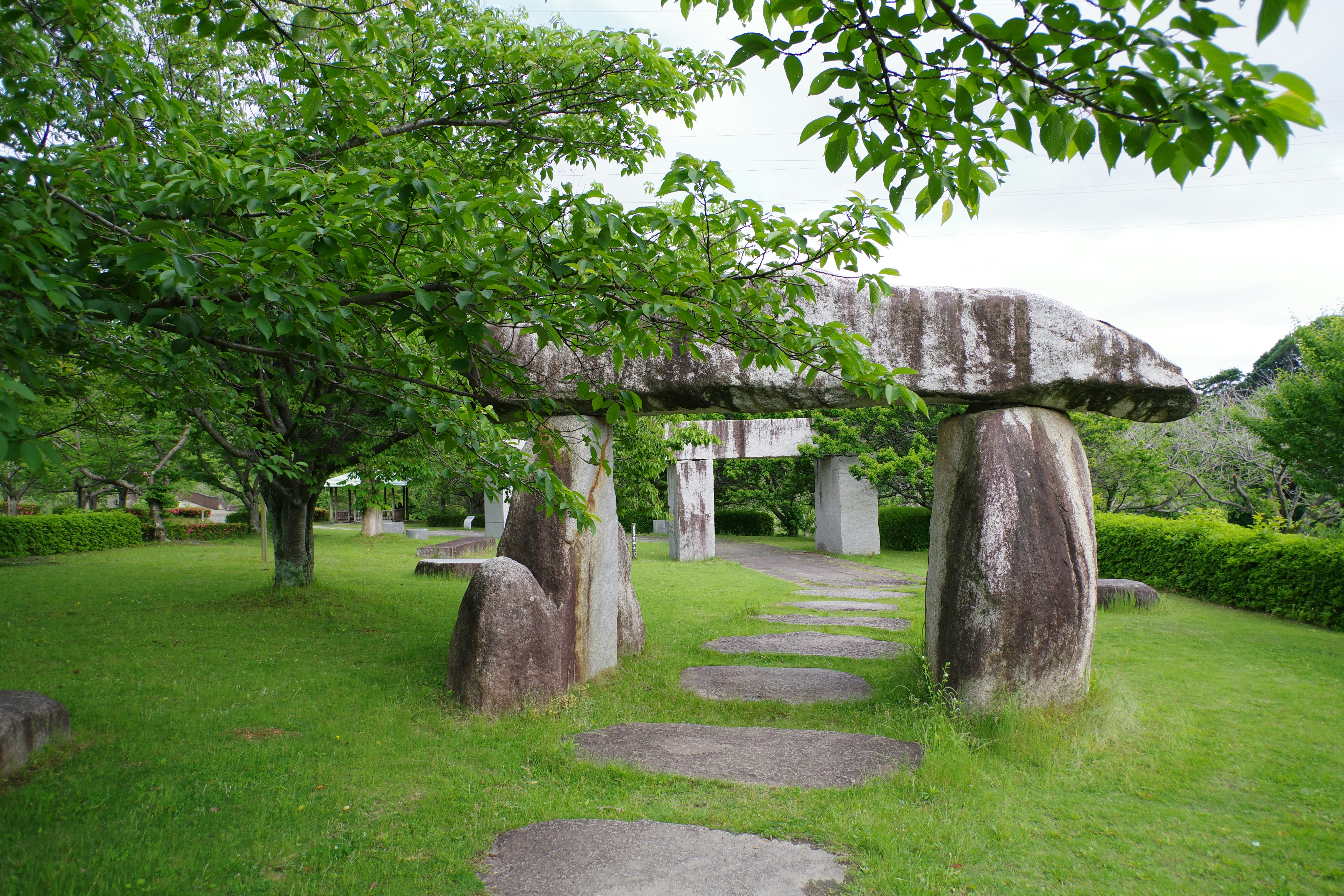 A stone arch in a grassy area next to trees