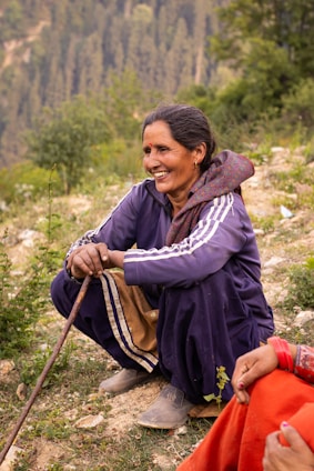 A woman sitting on top of a hill next to a forest