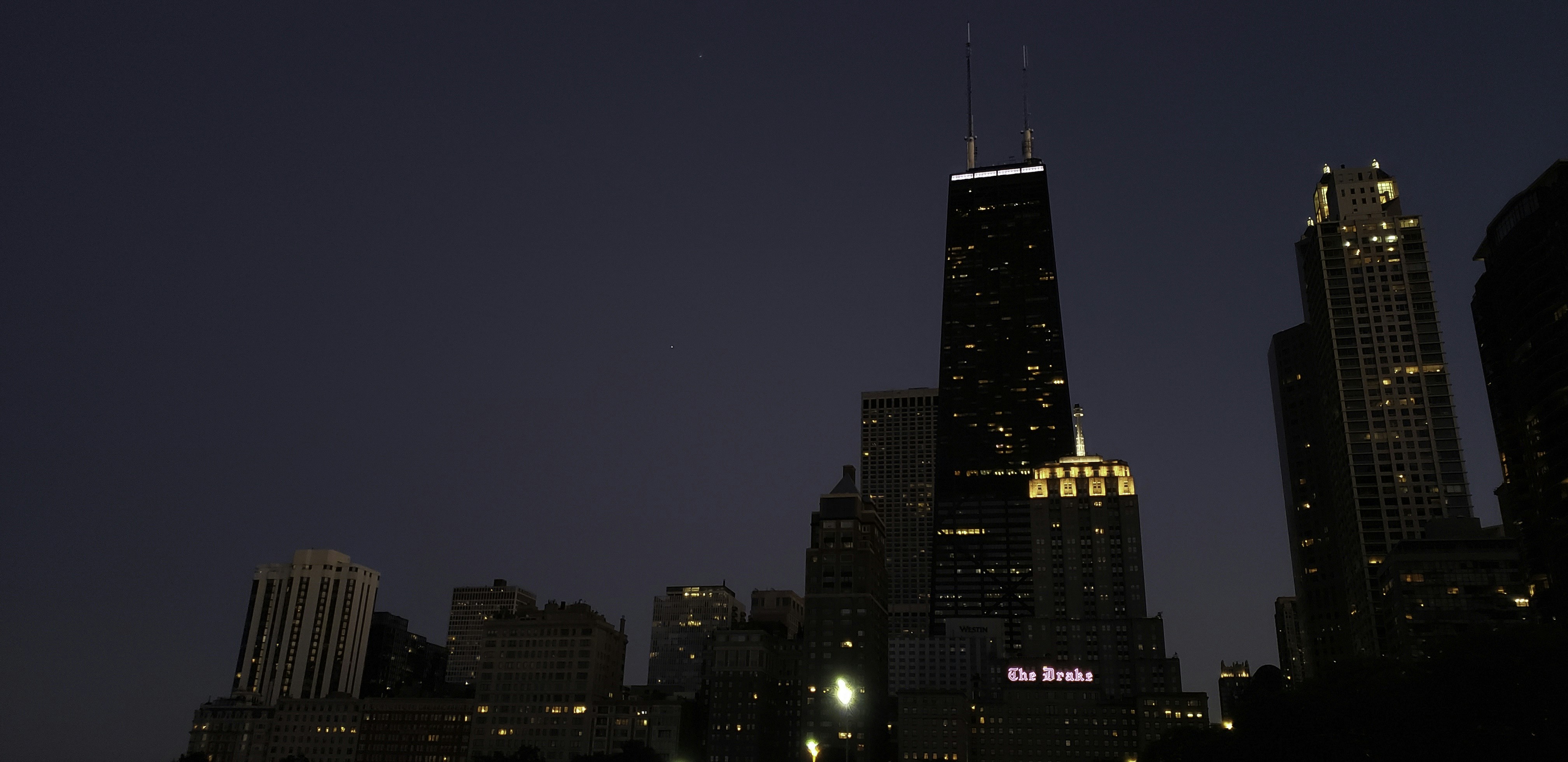 City skyline at dusk with dark silhouettes of buildings against deep navy sky, low ambient light, urban financial district