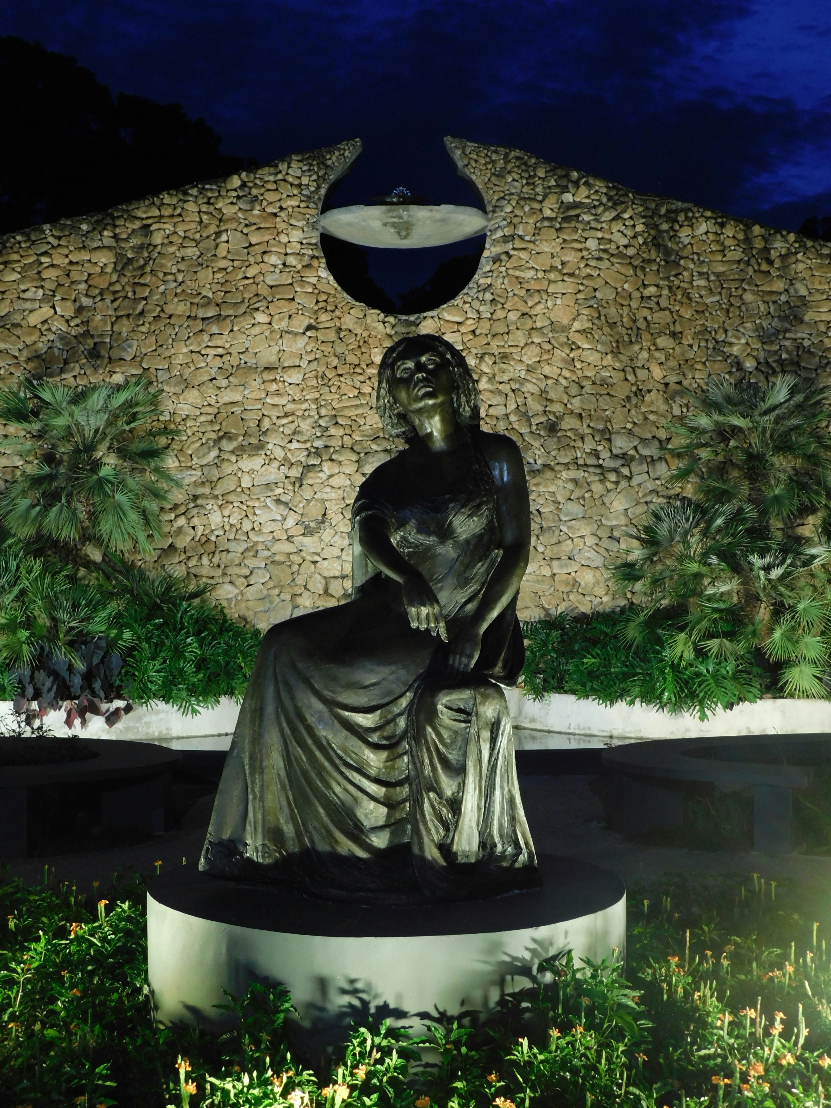 Uma estátua de uma mulher sentada em frente a uma cabana de palha