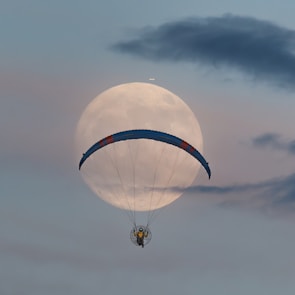 A person is parasailing in front of a full moon