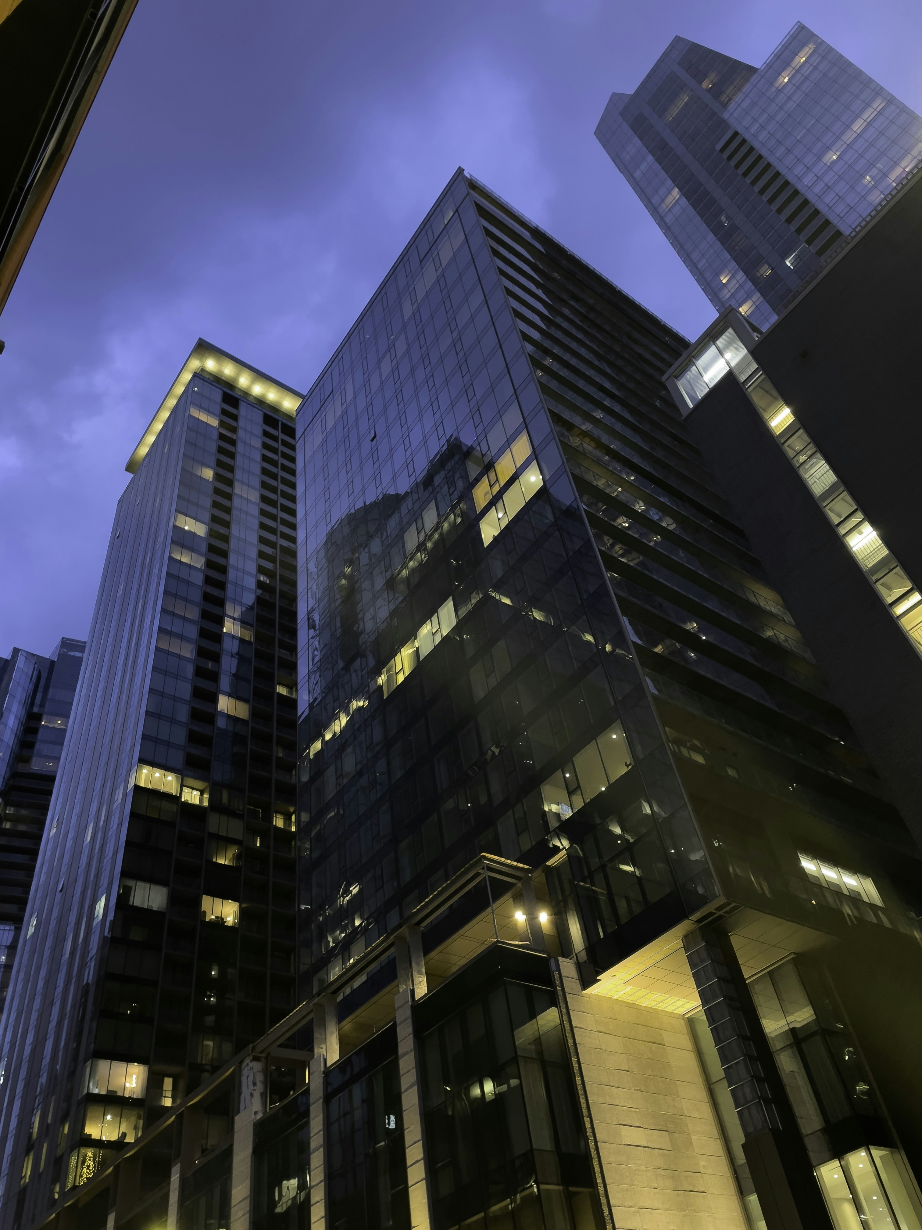 Modern glass skyscraper towers against twilight sky, deep blue-black atmosphere, city lights below, premium architectural photography