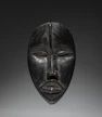 A dark wooden tribal mask with closed eyes.