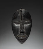 A dark wooden tribal mask with closed eyes.