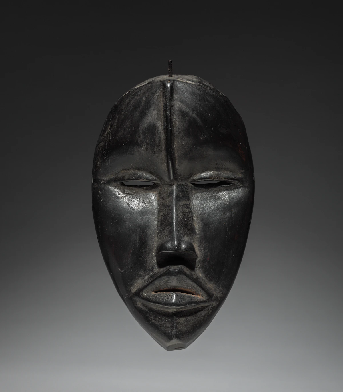 A dark wooden mask with closed eyes displayed in the gallery