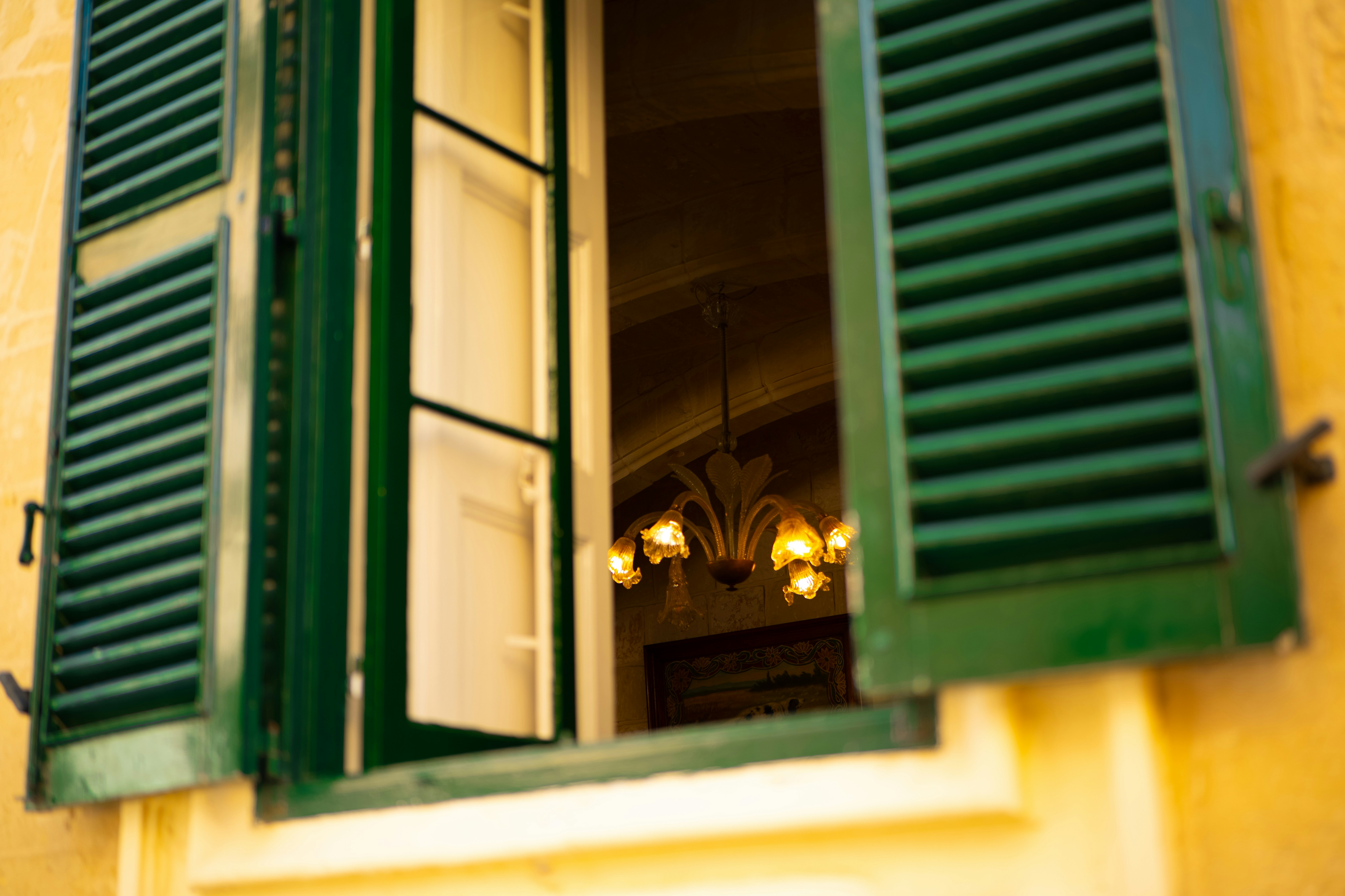 An open window with green shutters on a yellow building