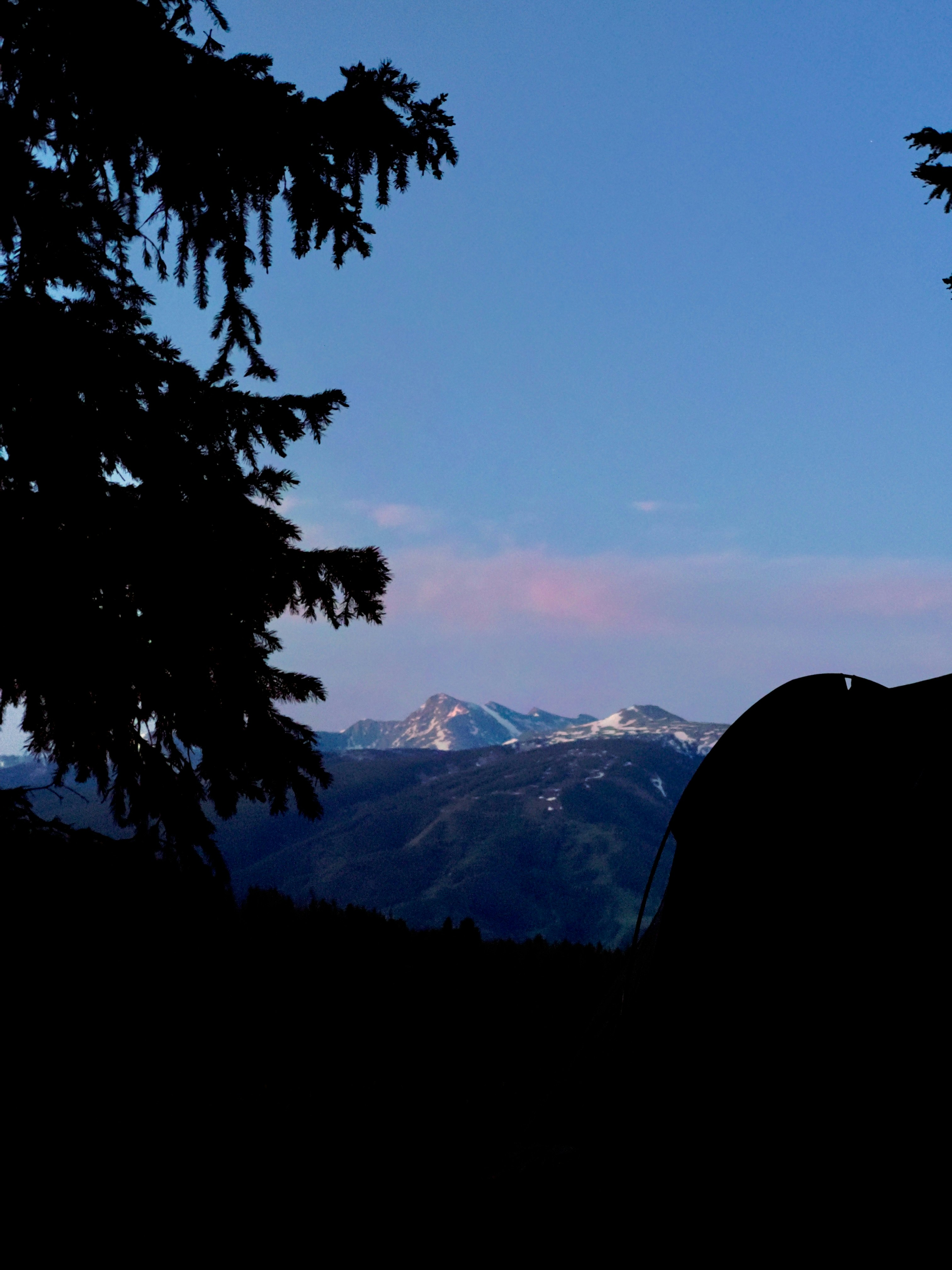 A silhouette of a person sitting on a rock with mountains in the background