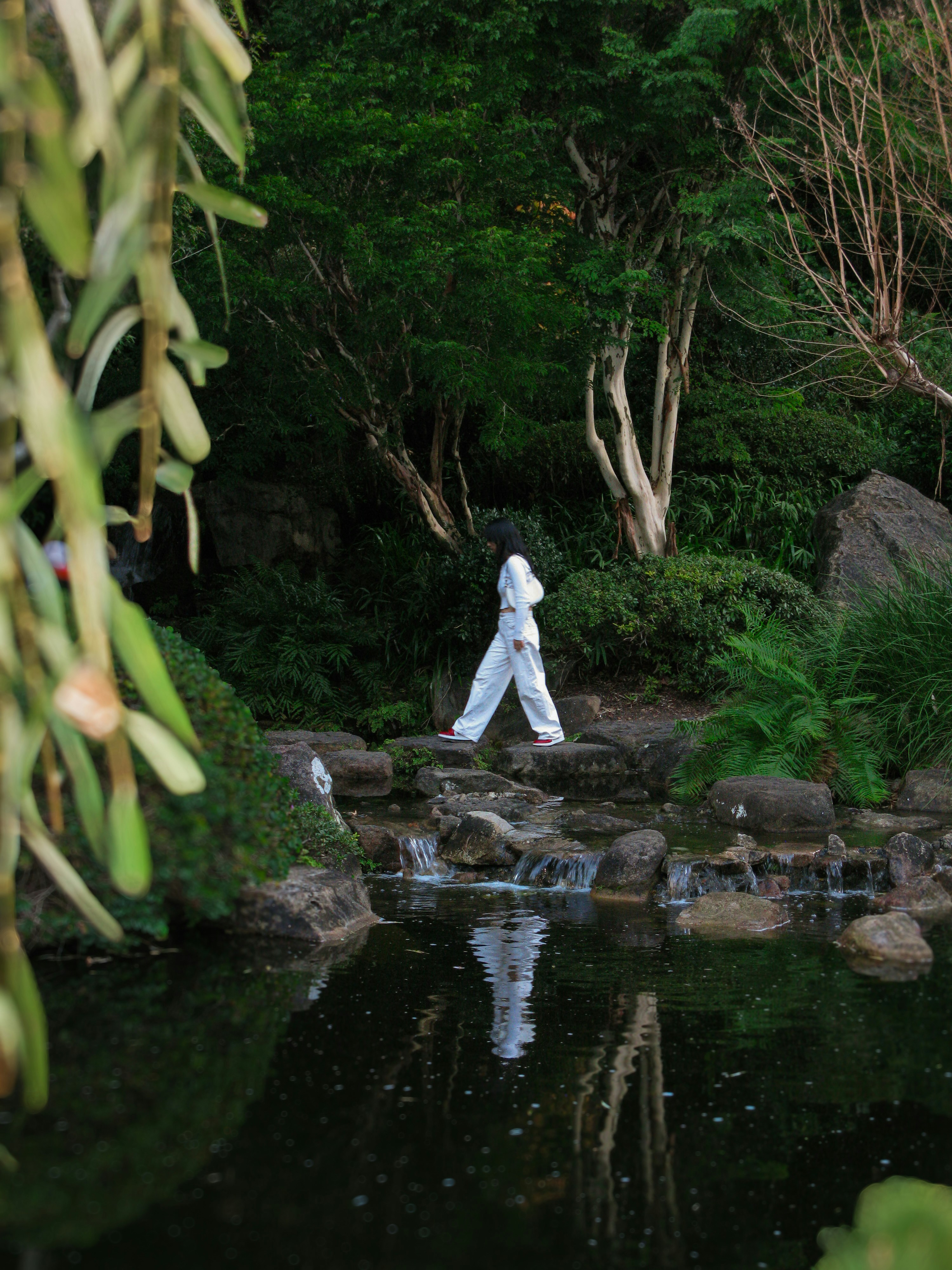 A man walking across a river next to a lush green forest