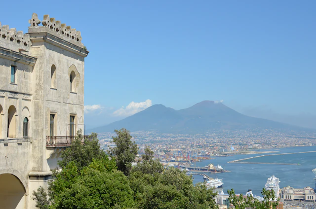 The cream-stone wall and arched windows of the Certosa di San Martino's belvedere, overlooking the Bay of Naples and Mount Vesuvius.