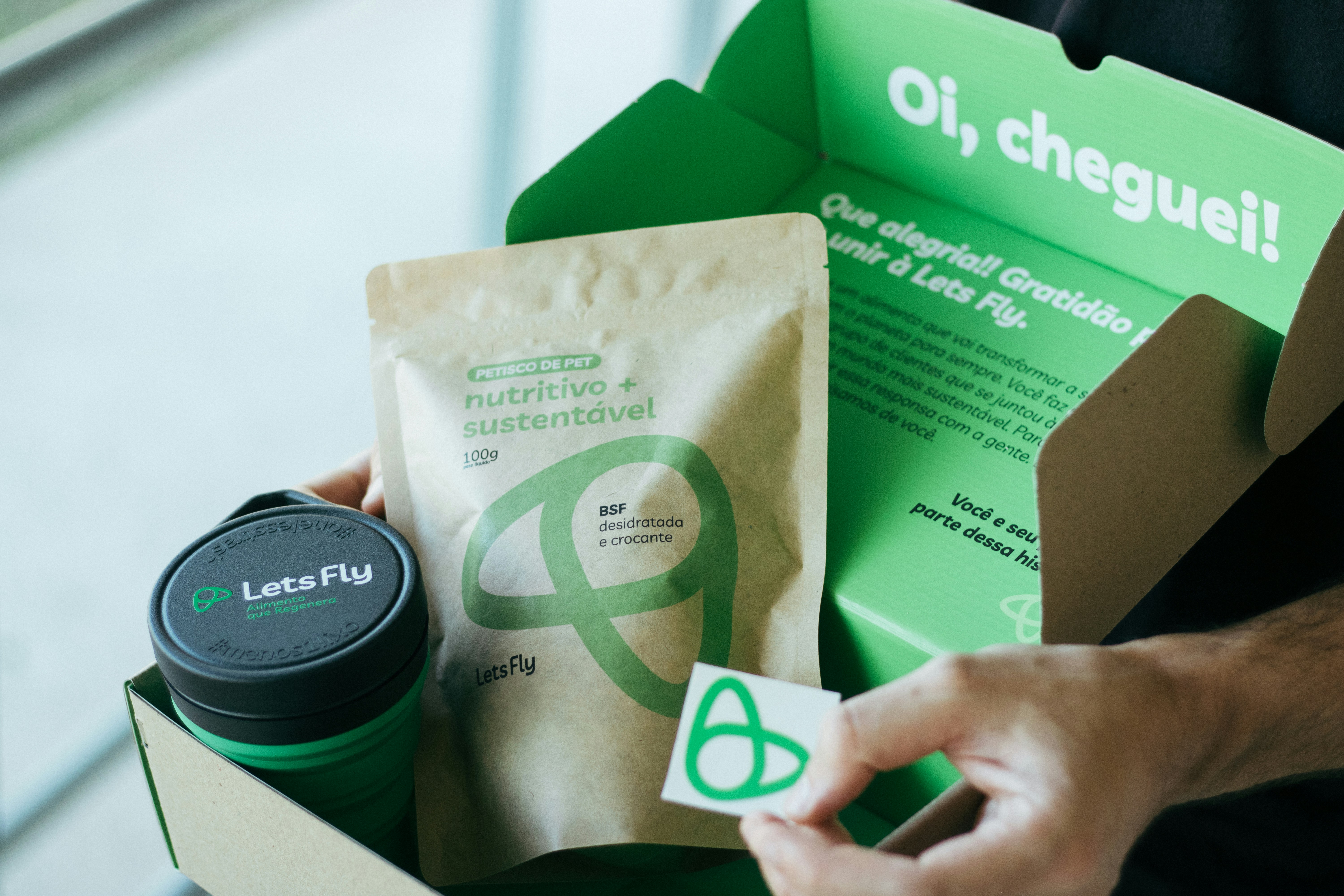 Hands hold an open box of sustainable pet products for the 'Lets Fly' brand.