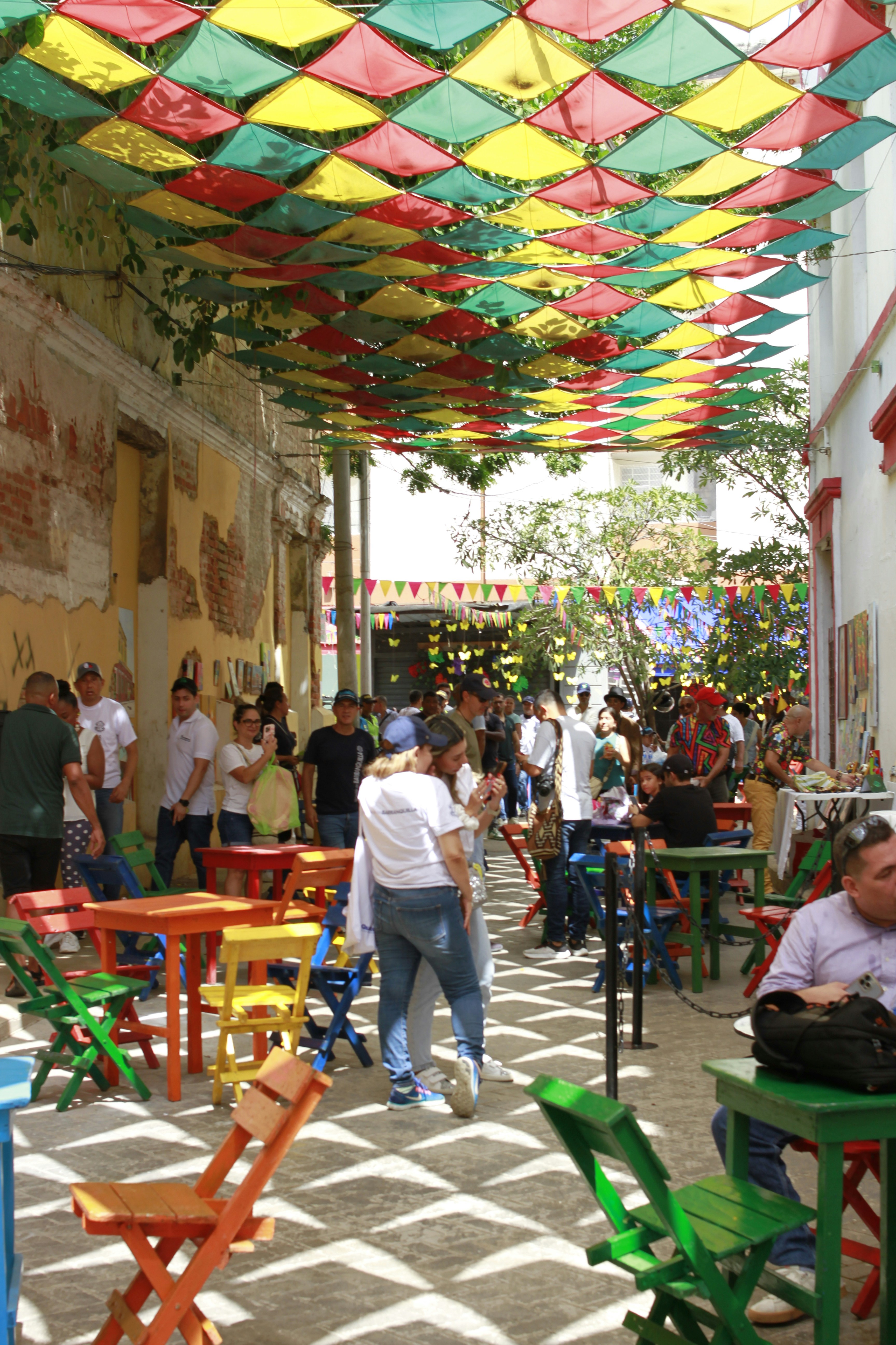 A group of people walking down a street next to tables and chairs