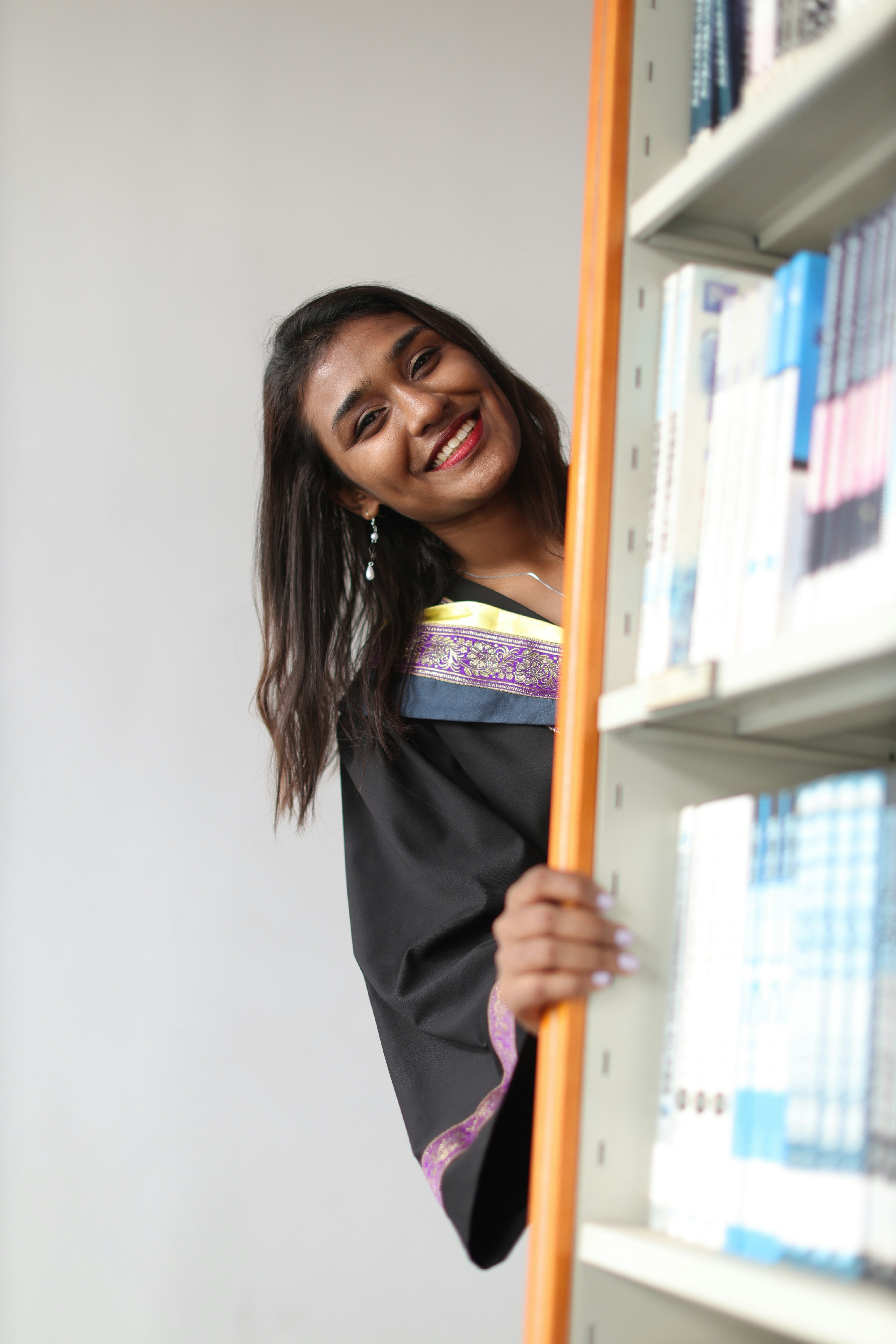 A woman leaning on a book shelf with a smile on her face