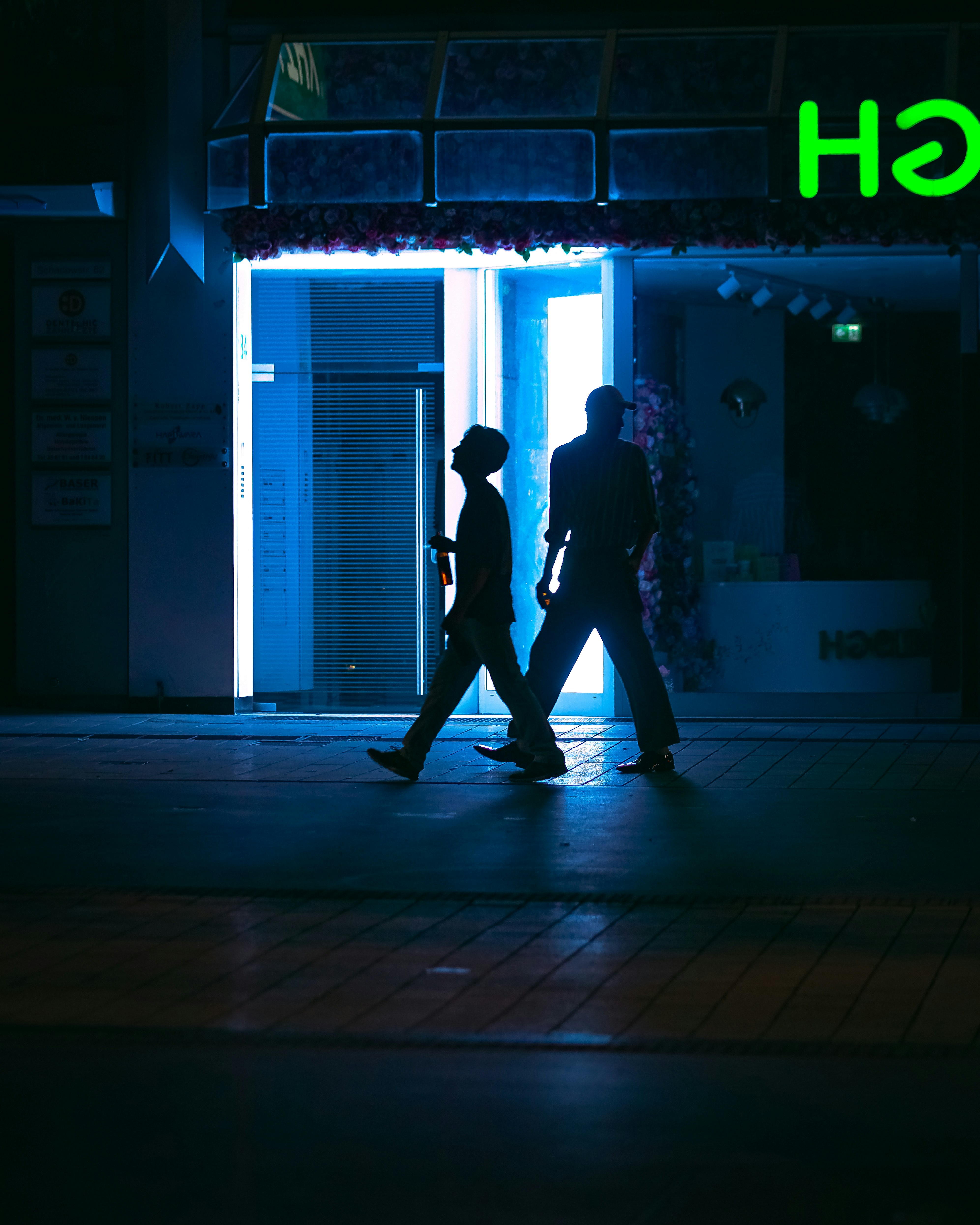 A couple of people walking down a street at night photo – Free Blue ...