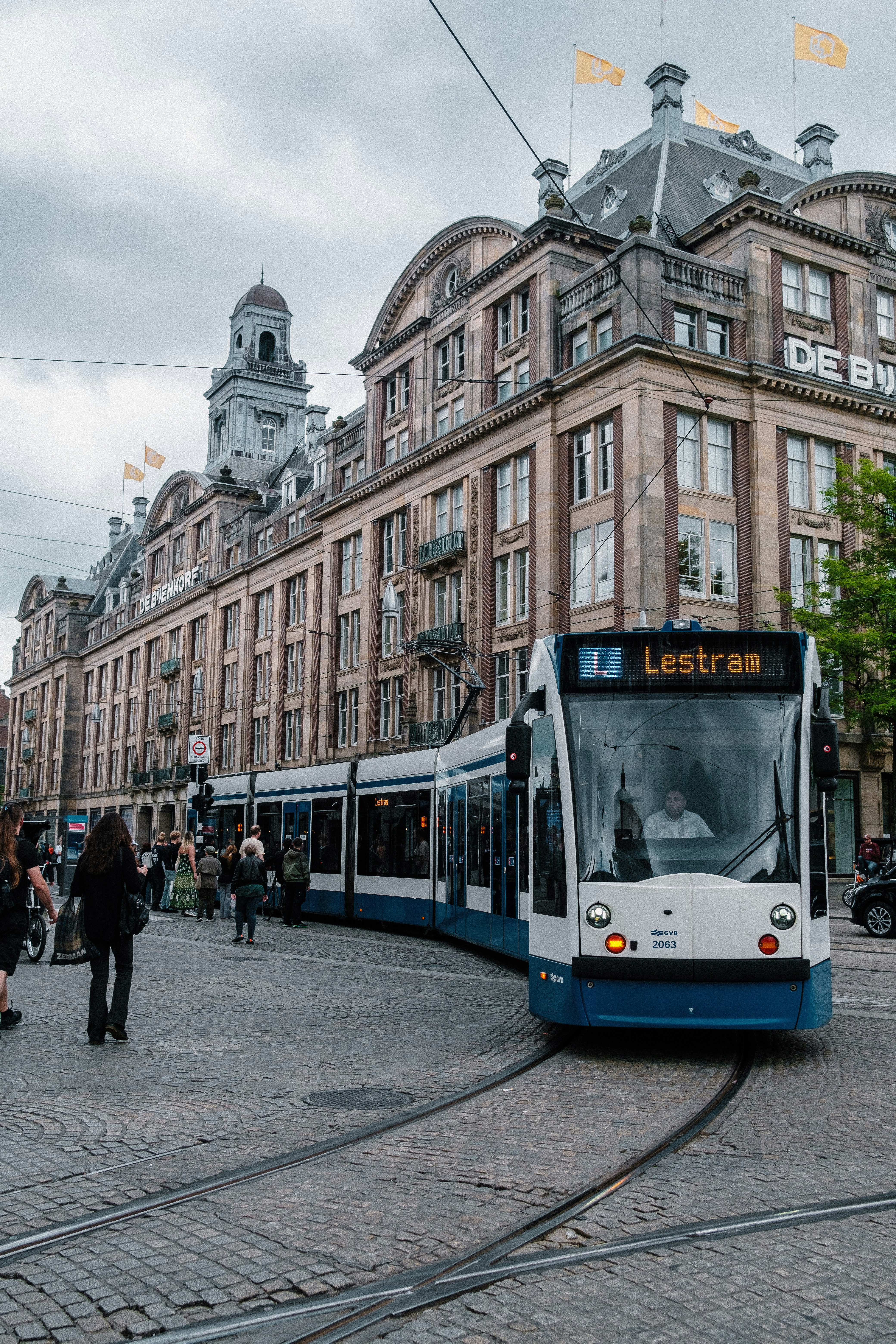 A blue and white train traveling down a street next to tall buildings