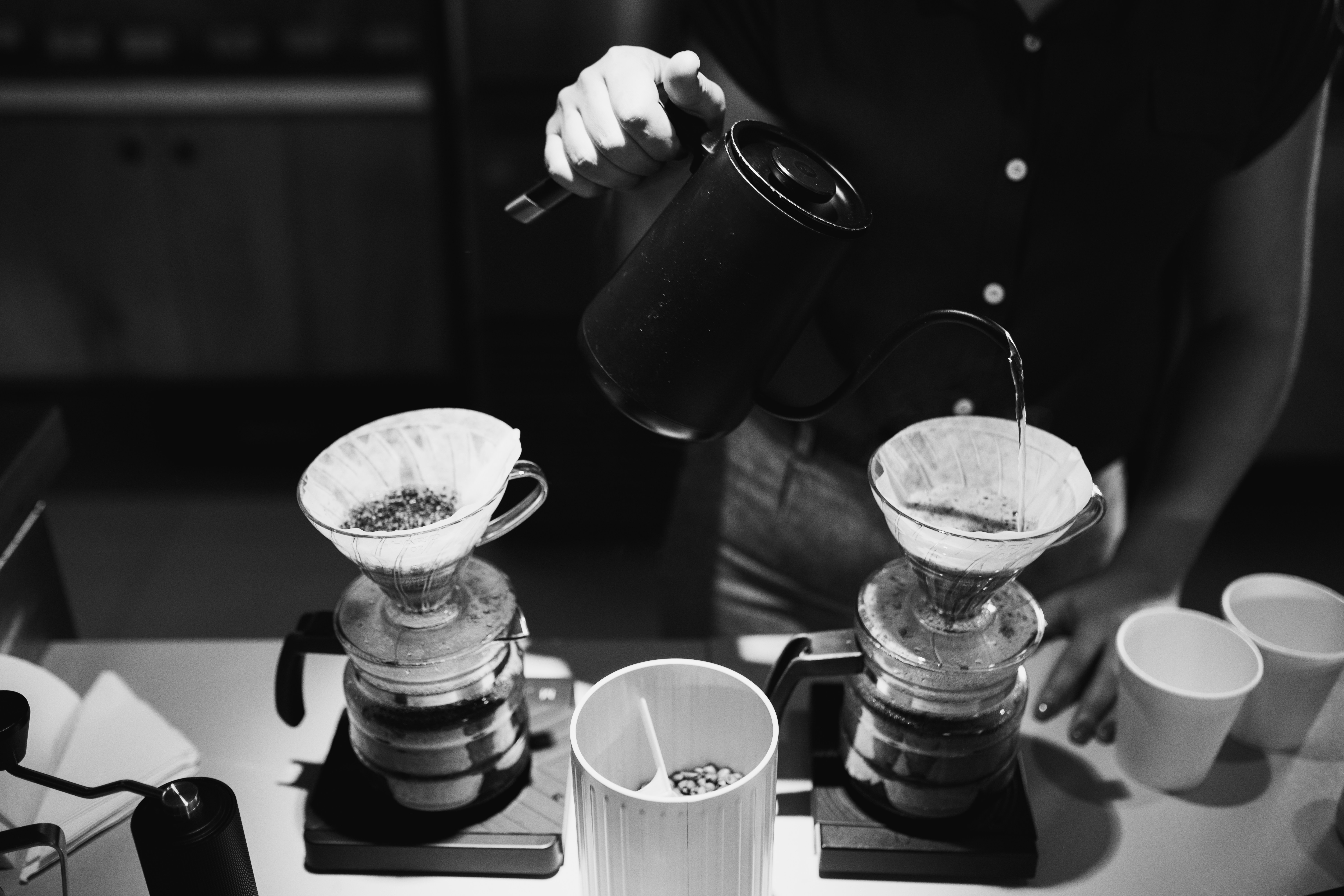Barista performing careful pour-over coffee technique with a gooseneck kettle over a glass carafe