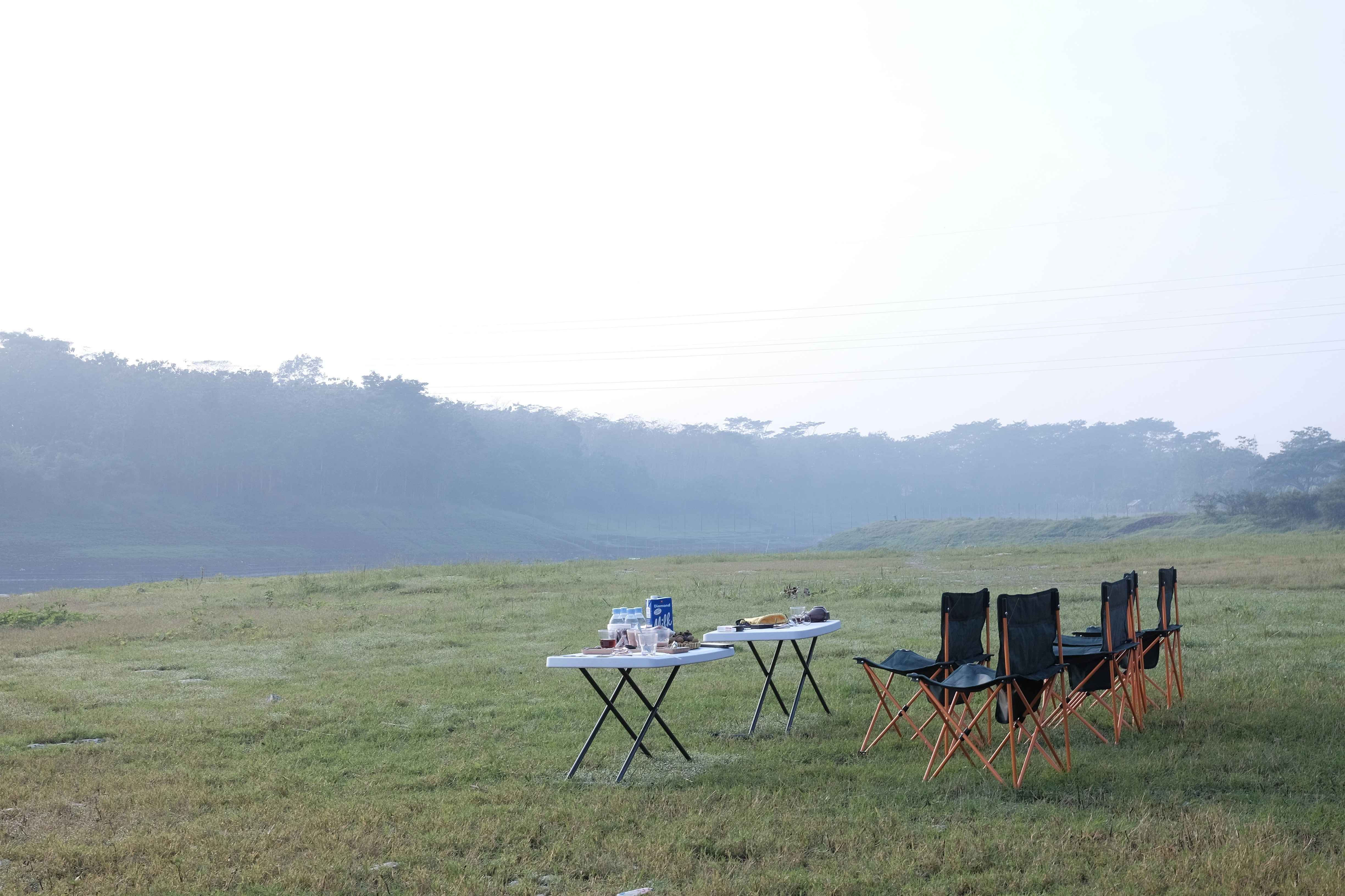 Camping tables and folding chairs arranged in an open outdoor campsite