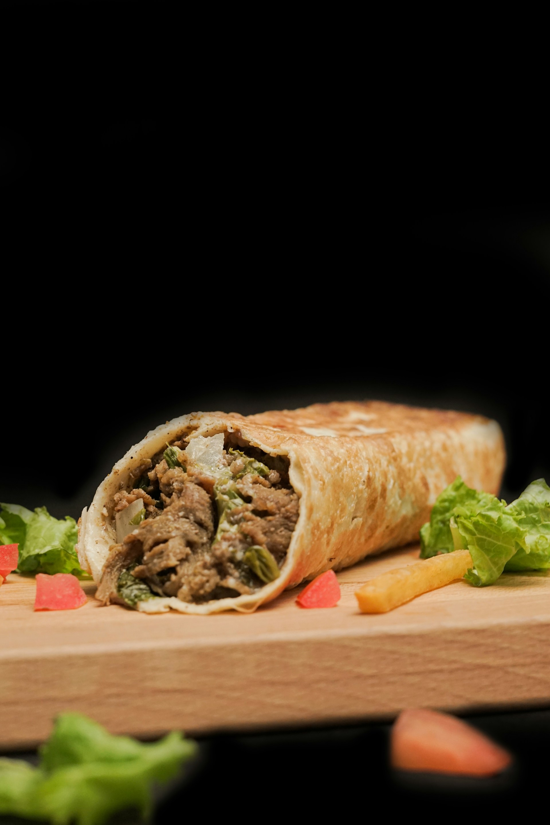 A burrito with meat and vegetables on a cutting board