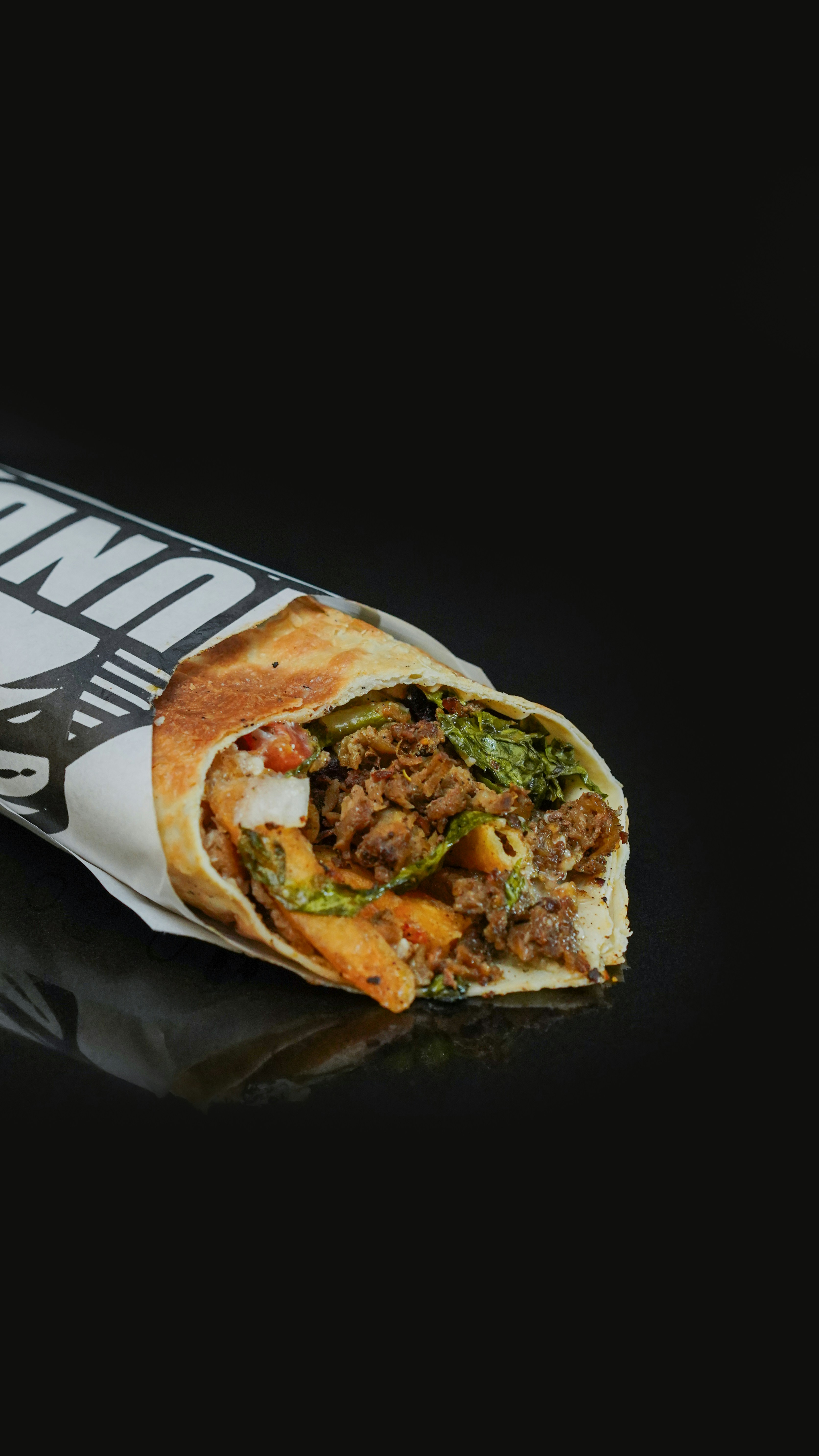 A burrito wrapped in a wrapper on a black background