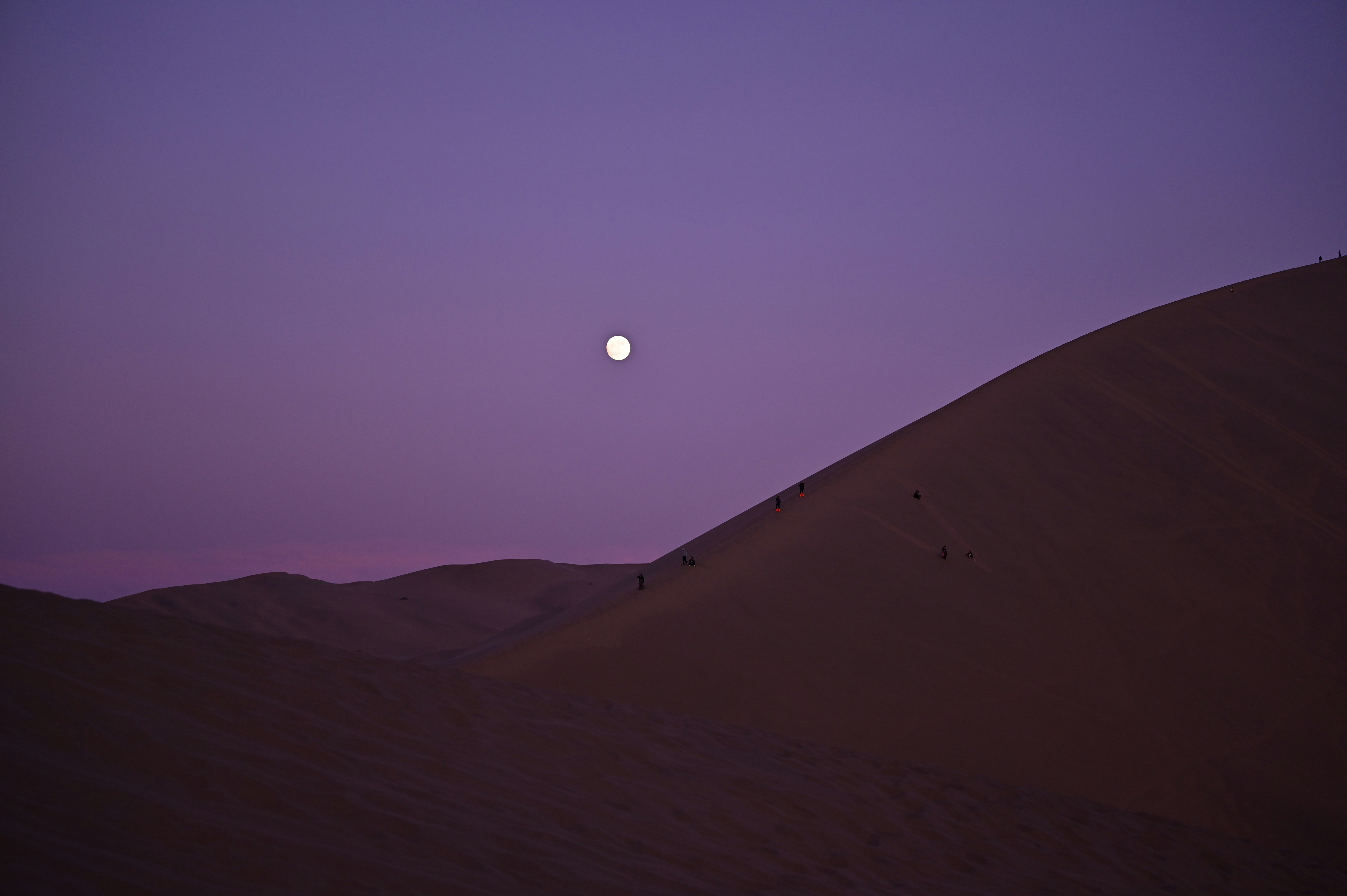 La lune se couche dans le ciel au-dessus des dunes de sable
