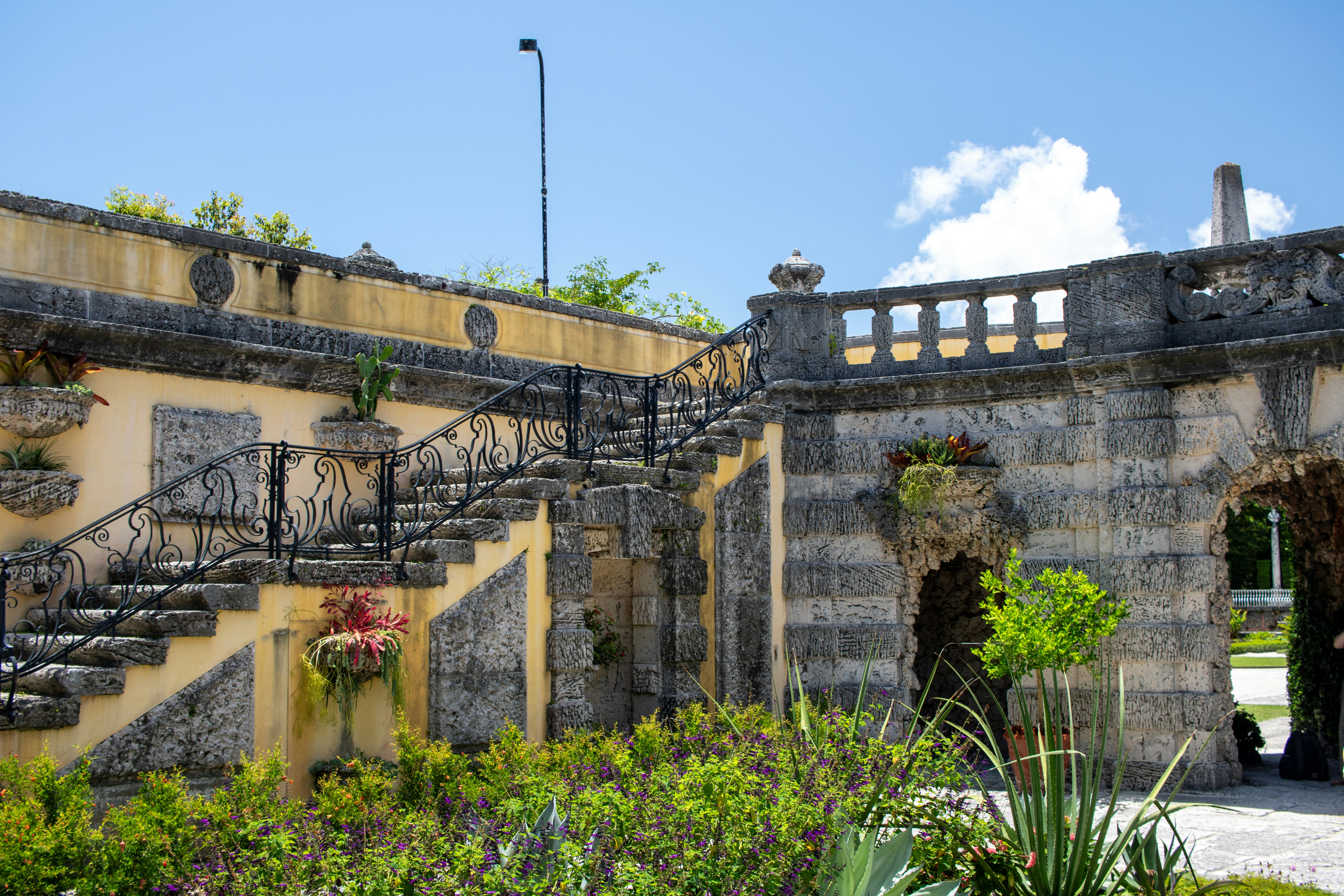 A stone building with a set of stairs leading up to it, Staircase at the Vizcaya Museum and Gardens, located in the Coconut Grove neighborhood of Miami, Florida, is an exquisite example of Mediterranean Revival architecture infused with Italian Renaissance influences. Built between 1914 and 1922 as the winter residence of industrialist James Deering, Vizcaya encompasses 34 decorated rooms filled with European antiques and art dating from the 16th to the 19th centuries.