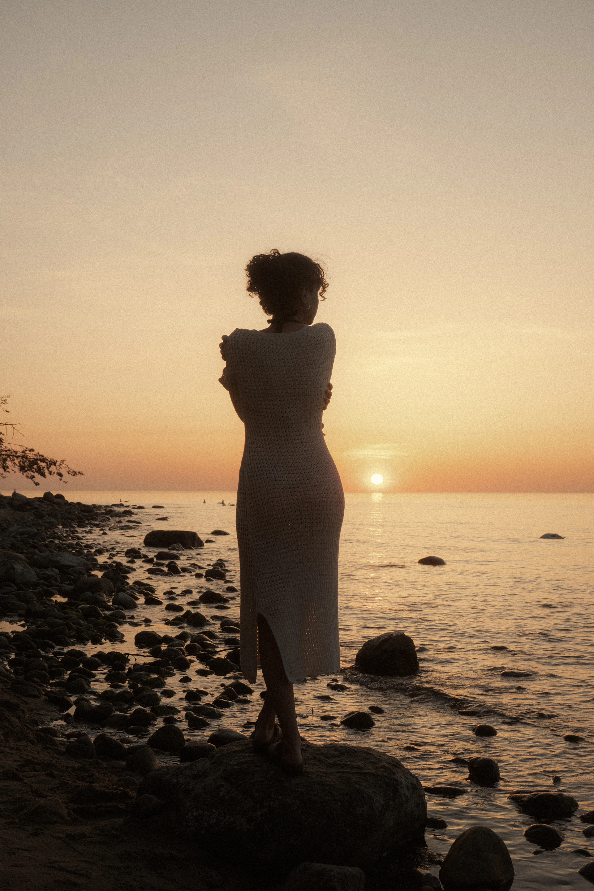 A woman standing on a rocky beach at sunset