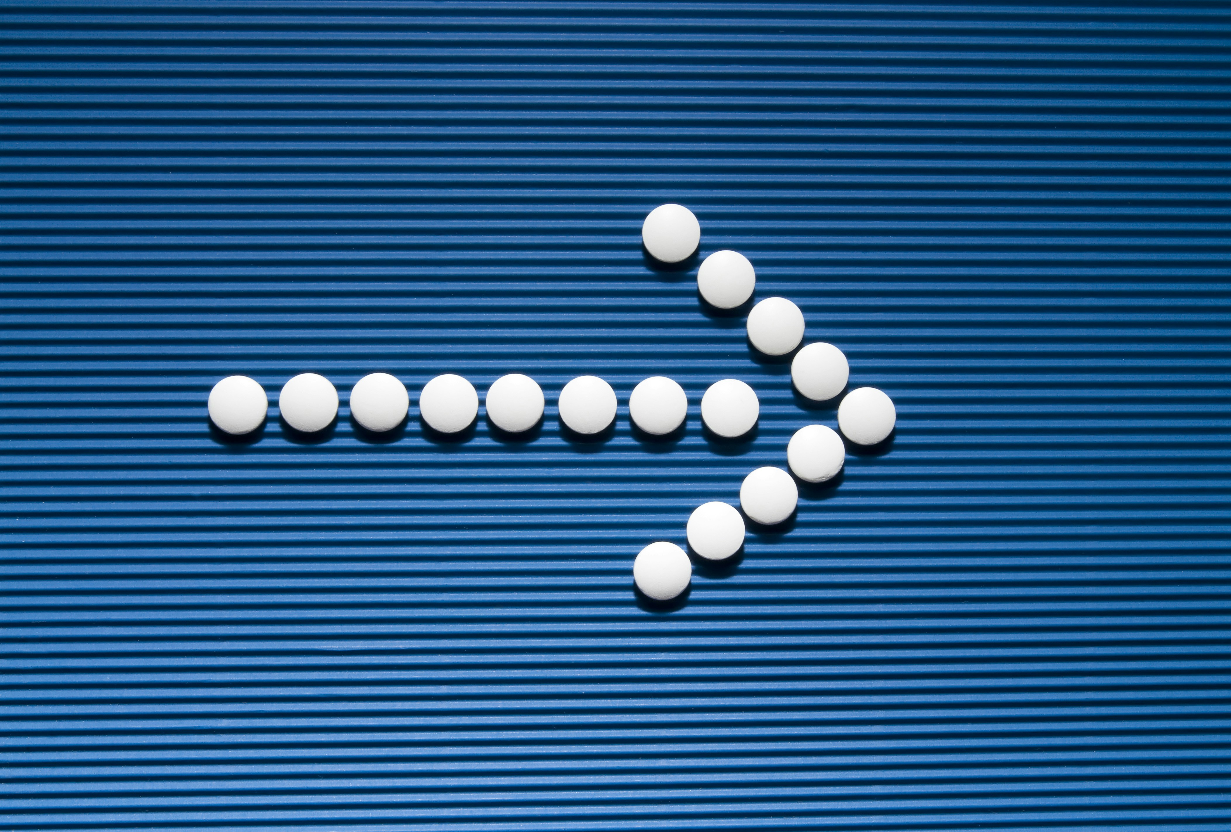 Pills are arranged in the shape of a cross on a blue background