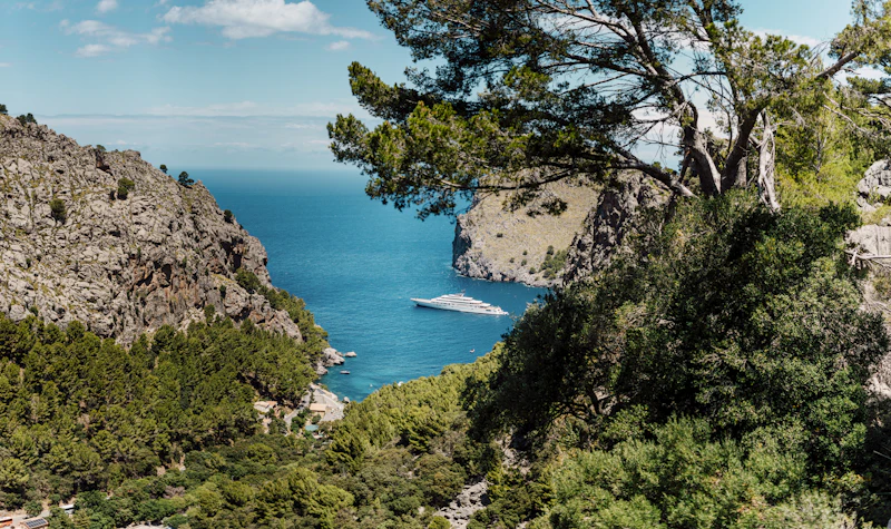 A narrow inlet at Sa Calobra on Mallorca's north coast, framed by pines and cliffs, a motor yacht at anchor