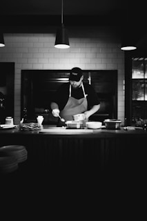 A black and white photo of a man cooking in a kitchen