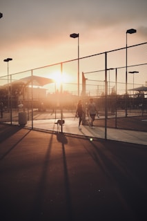 A couple of people walking down a street next to a fence