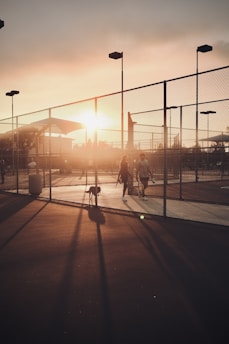 A couple of people walking down a street next to a fence