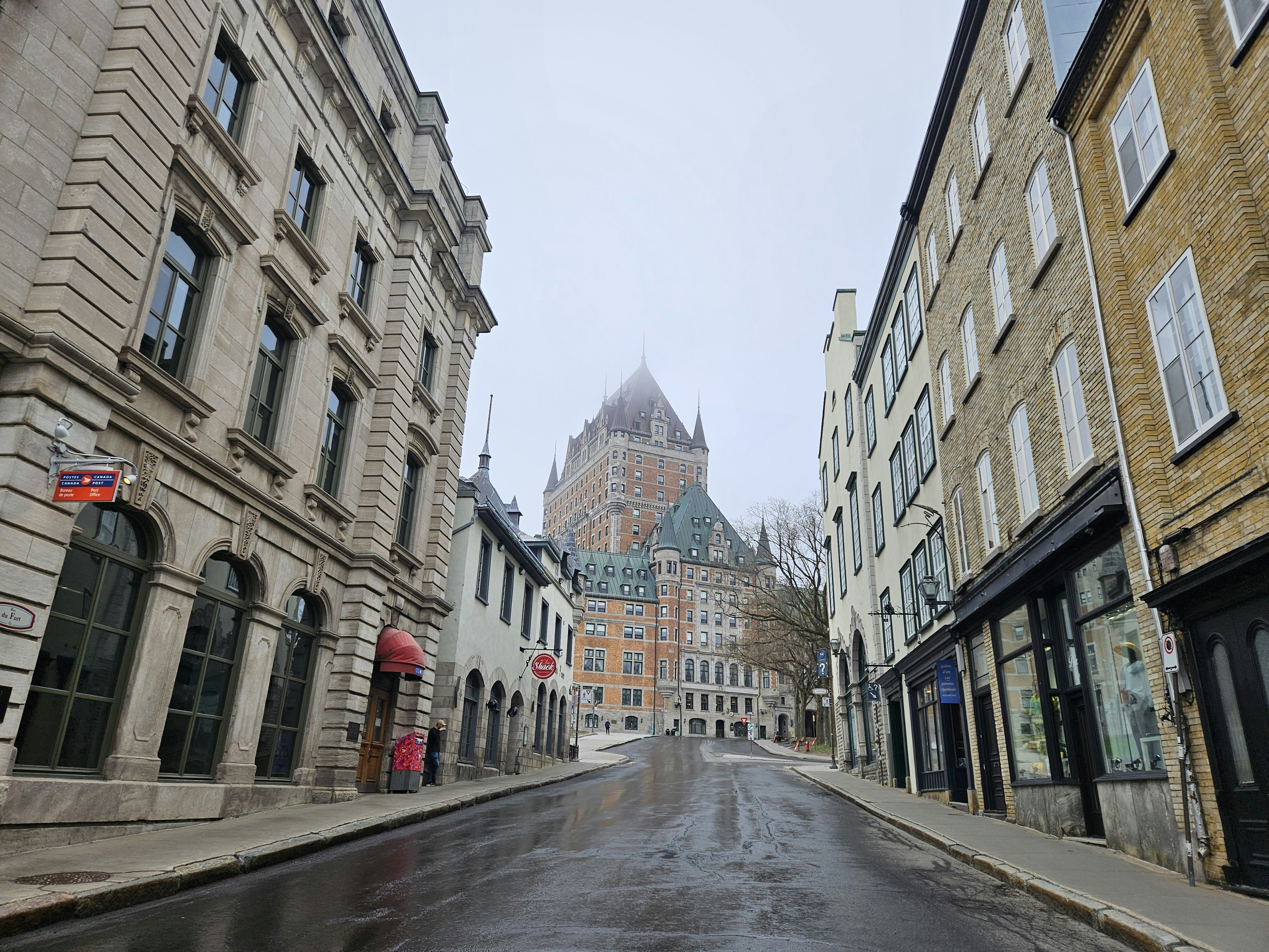 A wet street with buildings and a clock tower in the background