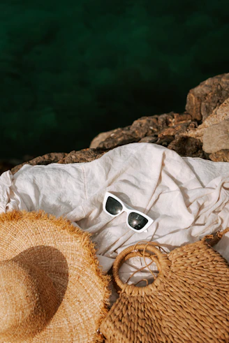 A hat, sunglasses, and a straw bag on a rocky beach