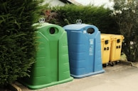 A row of trash cans sitting next to a bush