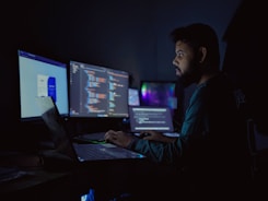 A man sitting in front of three computer monitors
