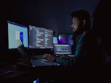 A man sitting in front of three computer monitors